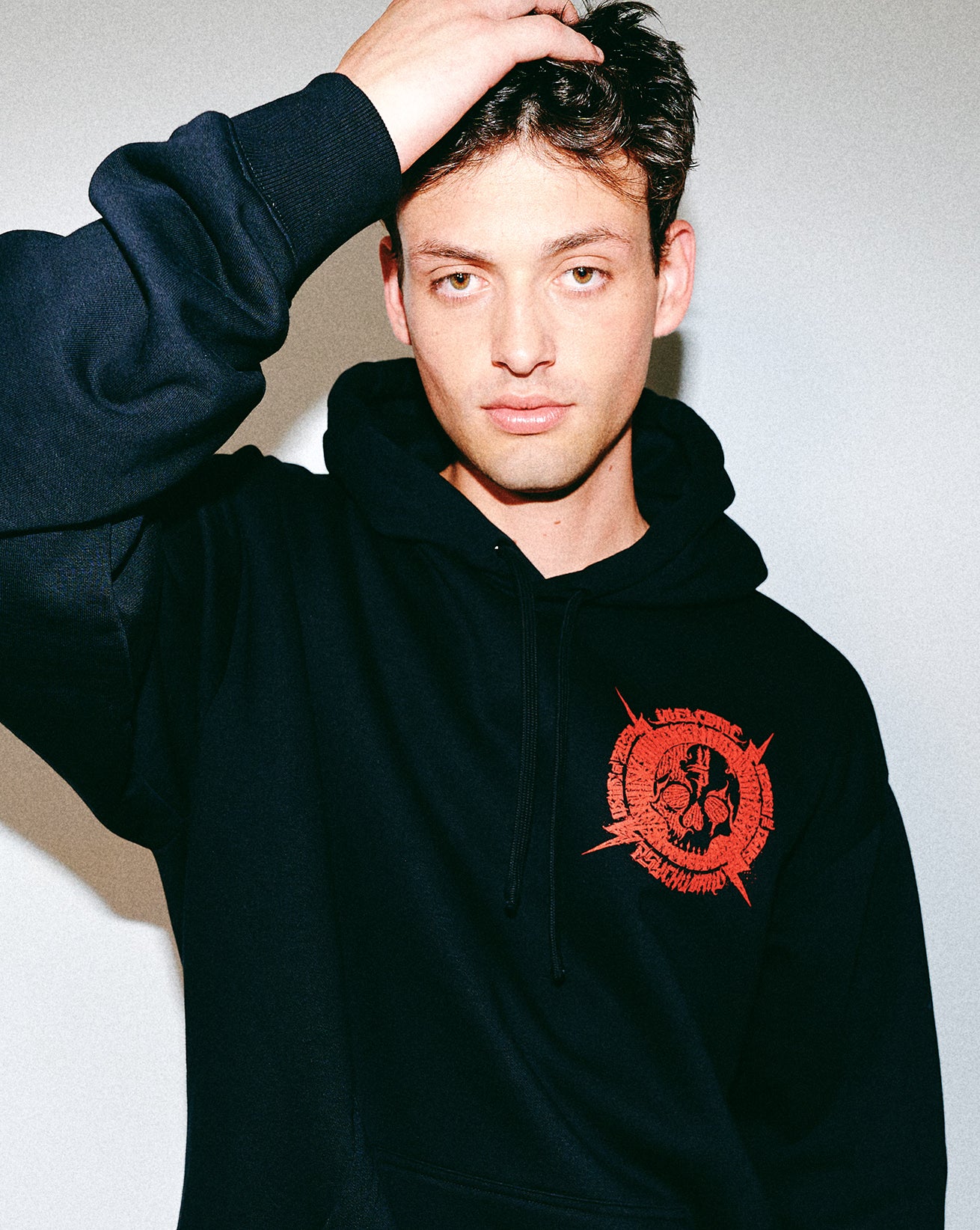 Person wearing a black hoodie with a red logo on a plain background