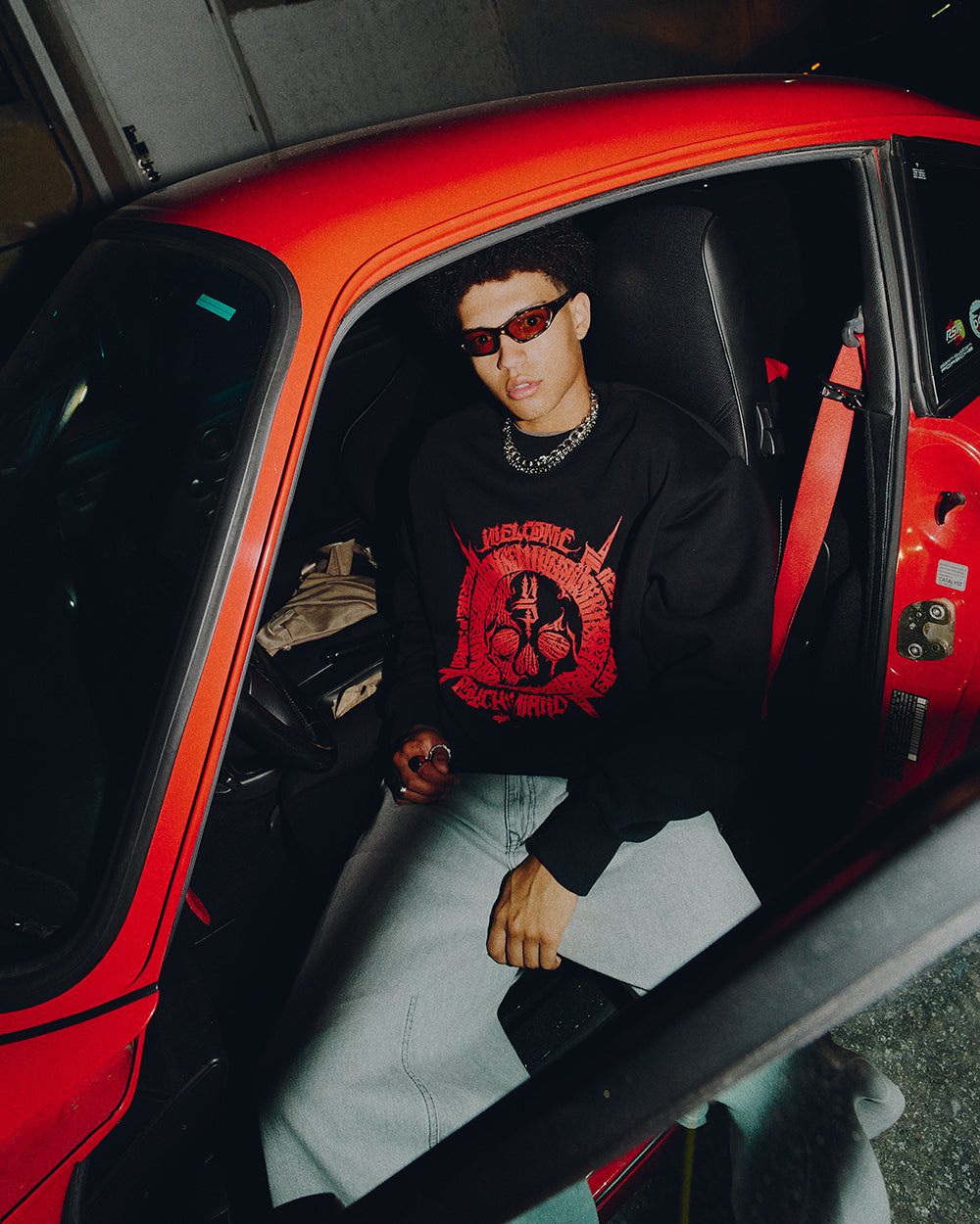 Person sitting inside a red car wearing a black sweatshirt with a red graphic design.