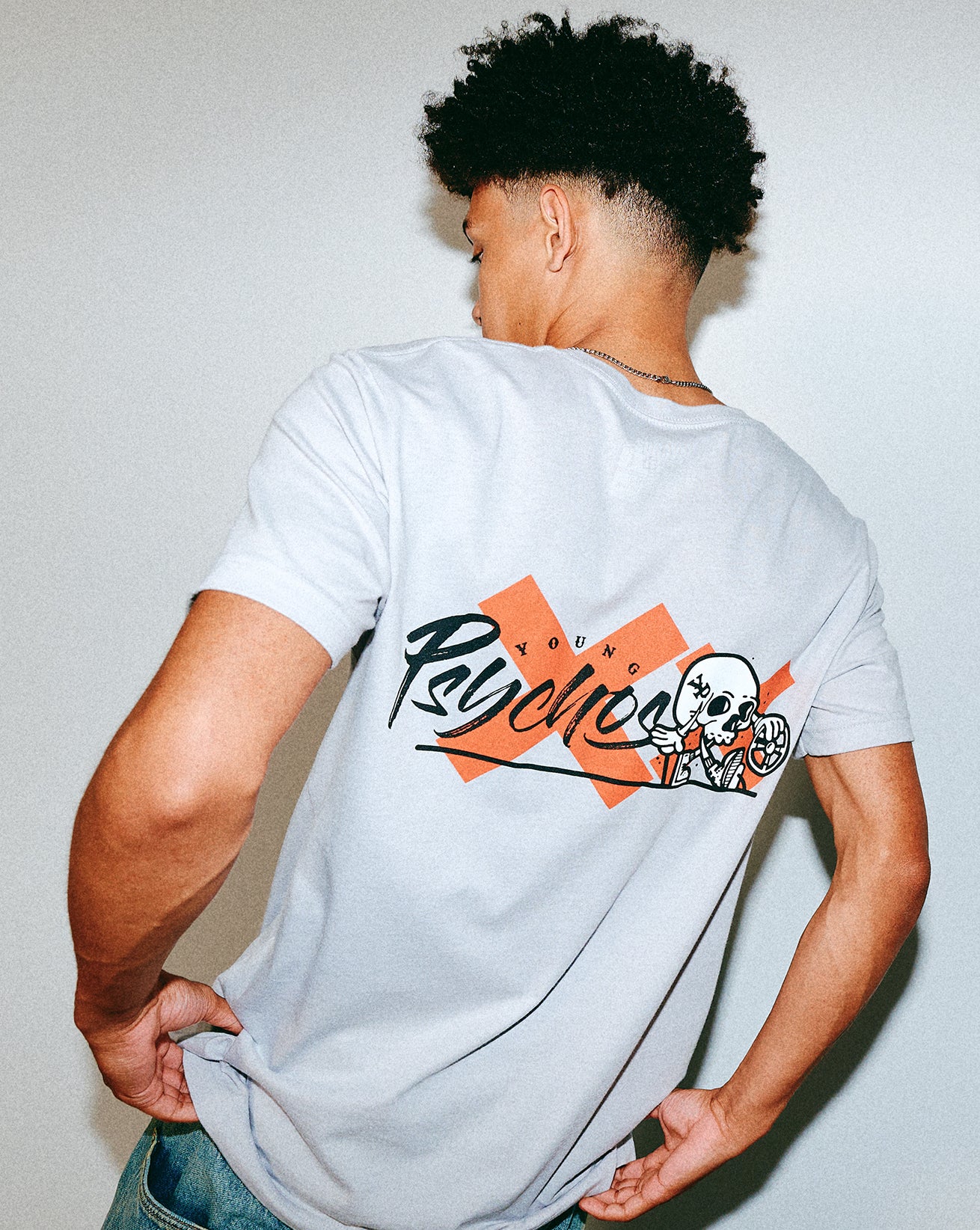 Person wearing a white t-shirt with a Young Psychos design on the back, standing against a plain background.