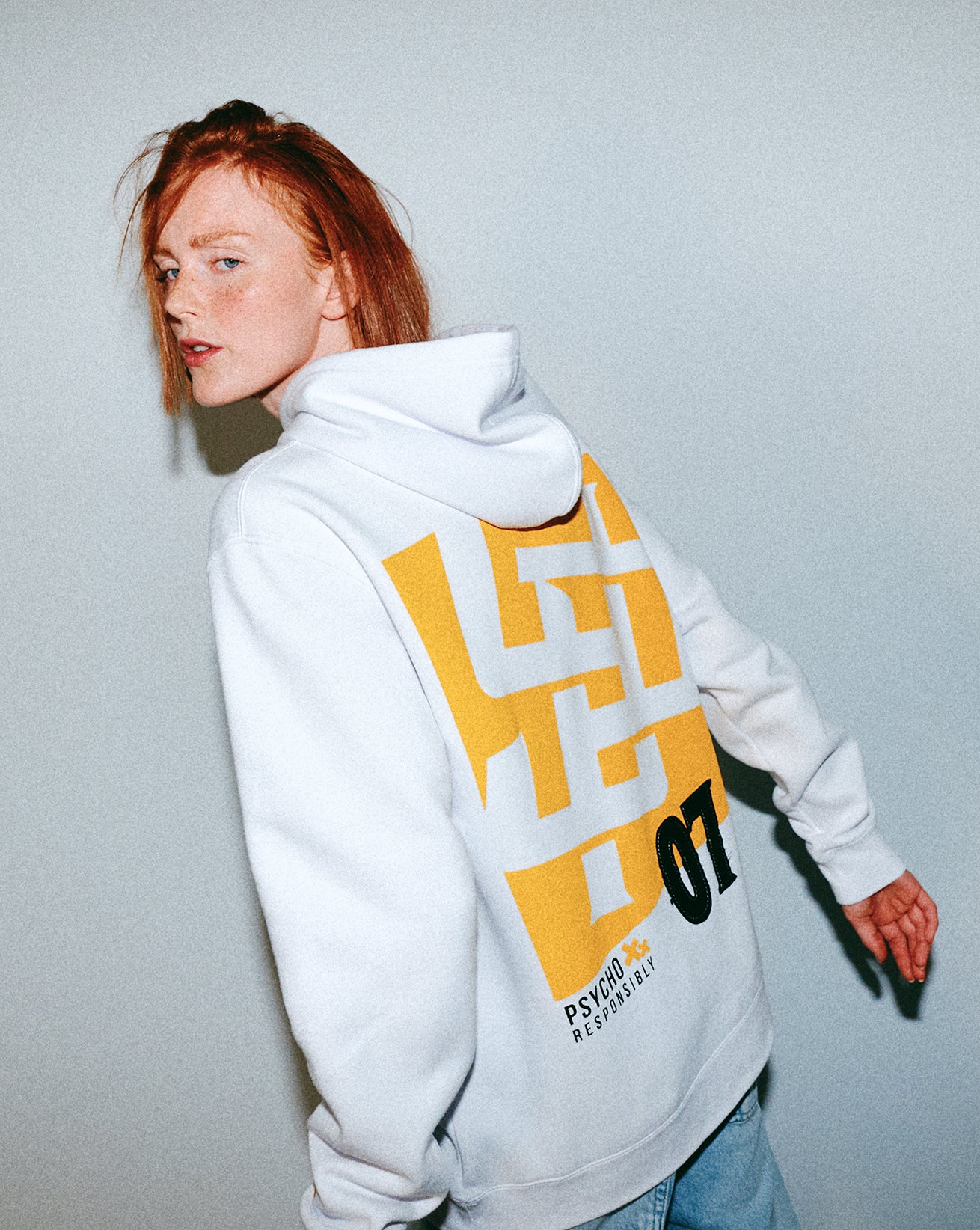 Person wearing a white hoodie with a yellow and black Young Psychos design on the back against a light gray background