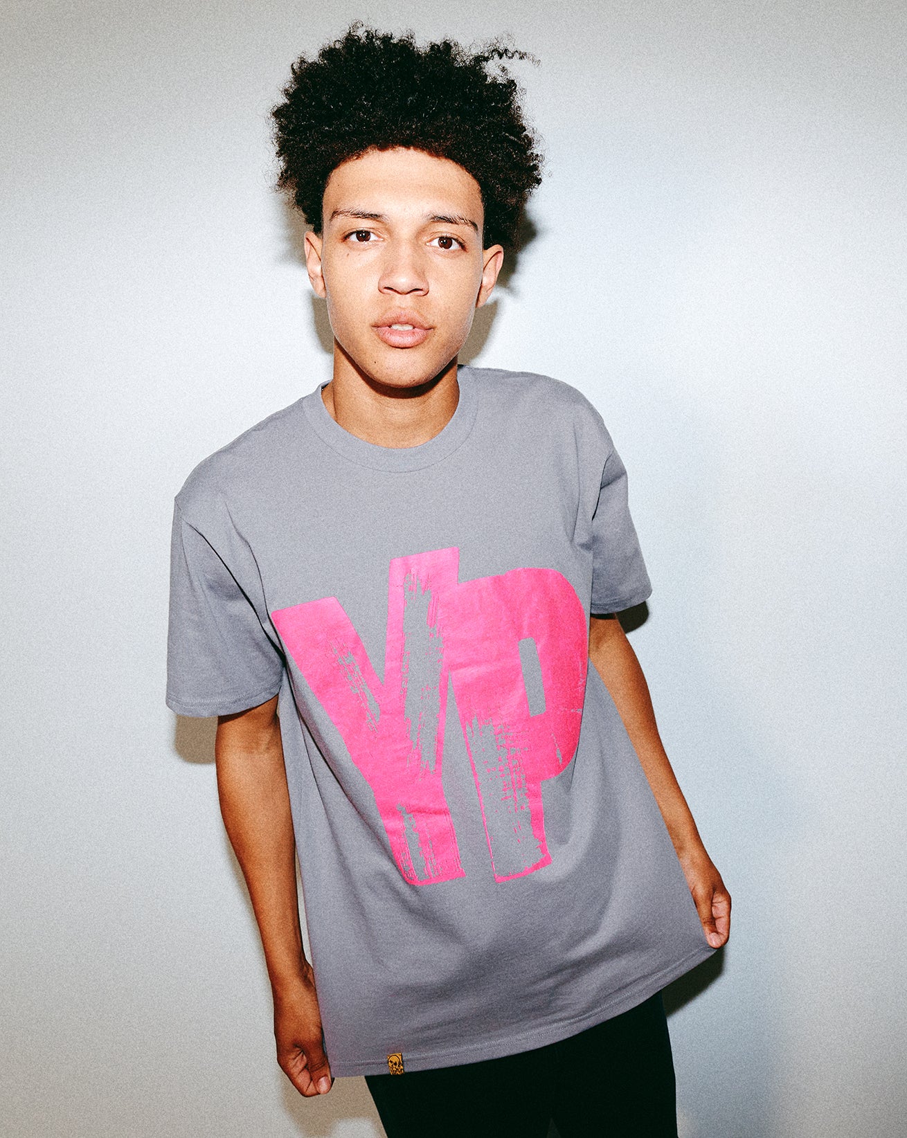 Person wearing a gray t-shirt with a pink Young Psychos text against a plain background