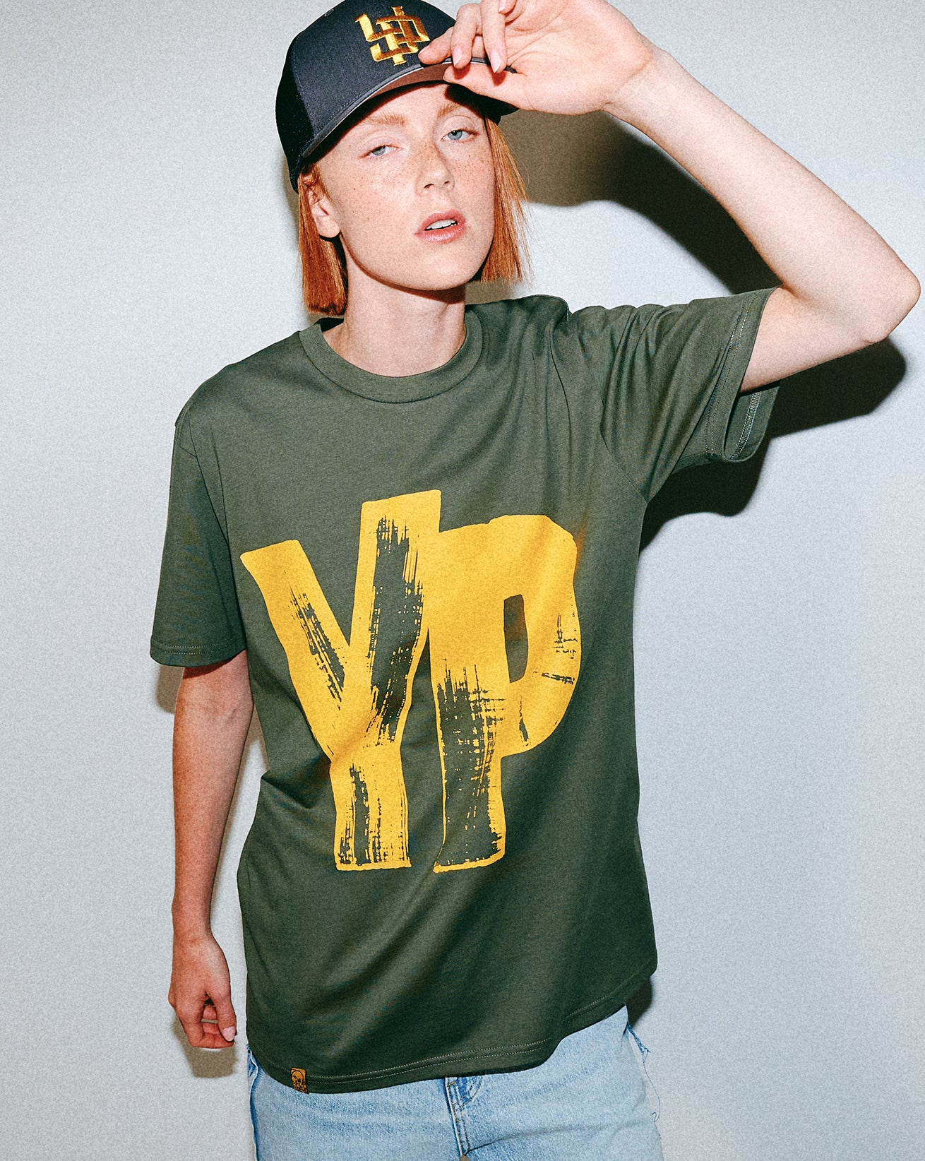 Person wearing a green t-shirt with yellow YP text and a cap, against a plain background