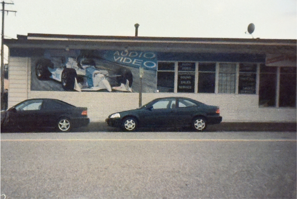 Two cars parked in front of a building with an 'Audio Video' sign.