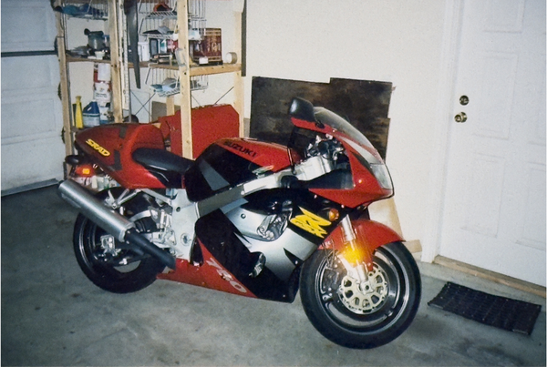 Red and black motorcycle parked in a garage with shelves and a door in the background.