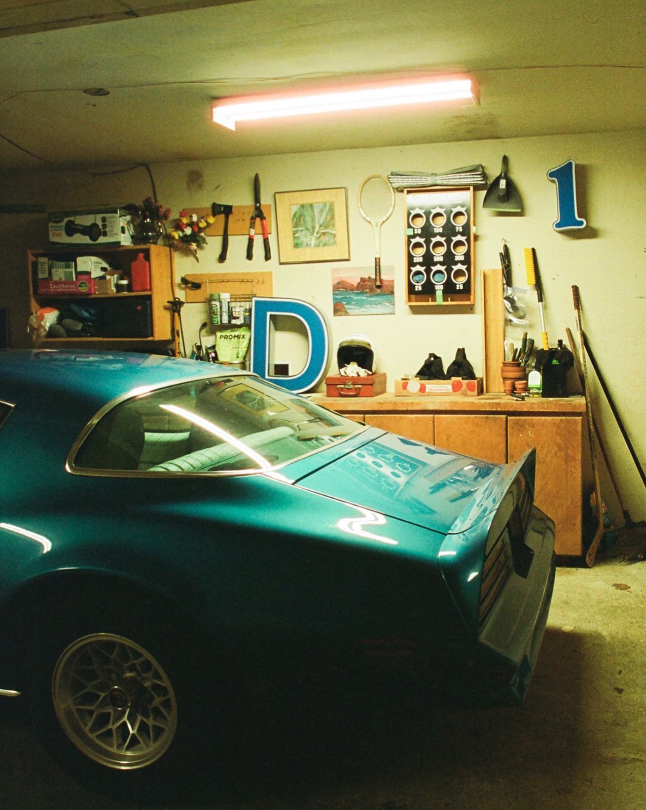 Teal car in a garage with various tools and equipment on the wall.