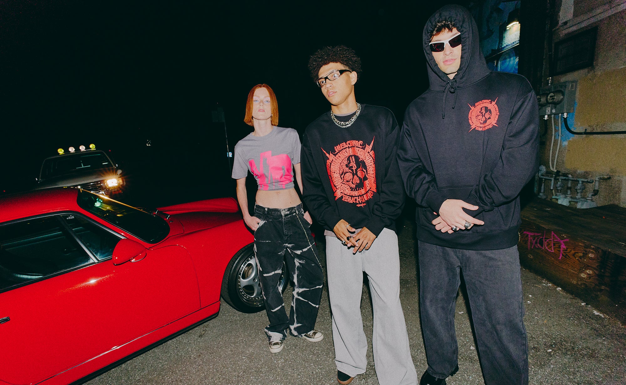 Three people standing next to a red car at night.