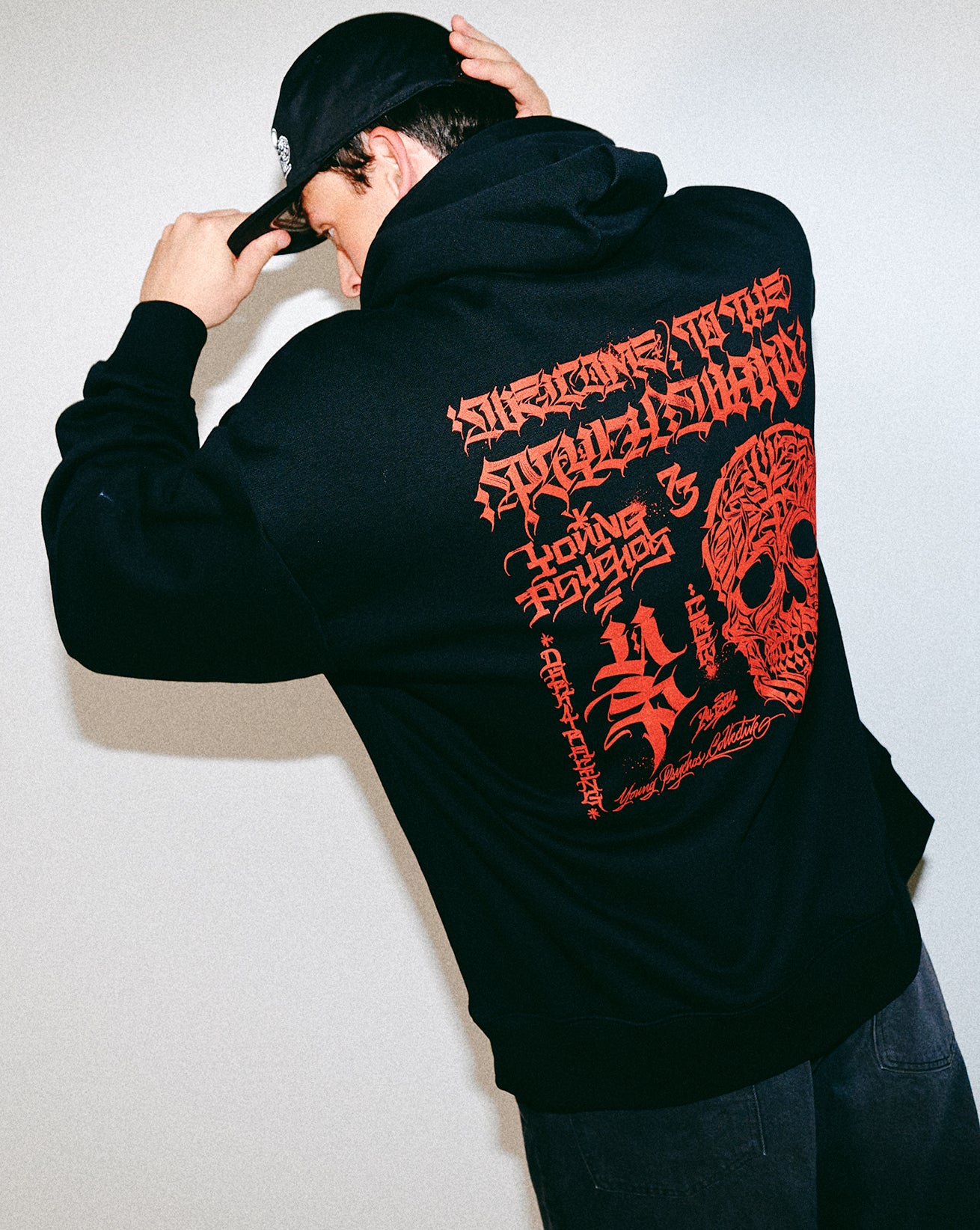 Person wearing a black hoodie with red text and skull design on the back, standing against a plain background.