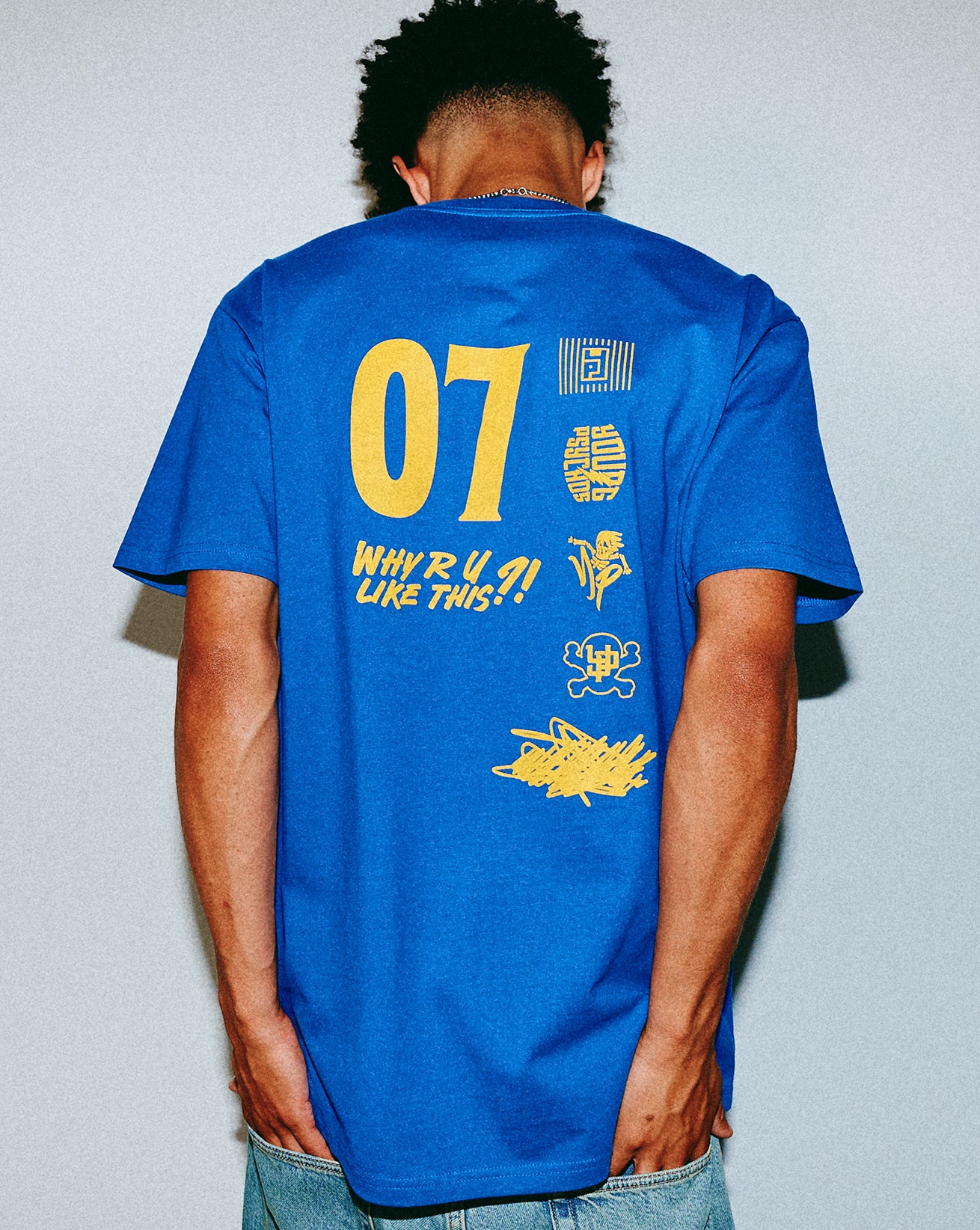 Person wearing a blue t-shirt with yellow text and graphics on the back against a plain background