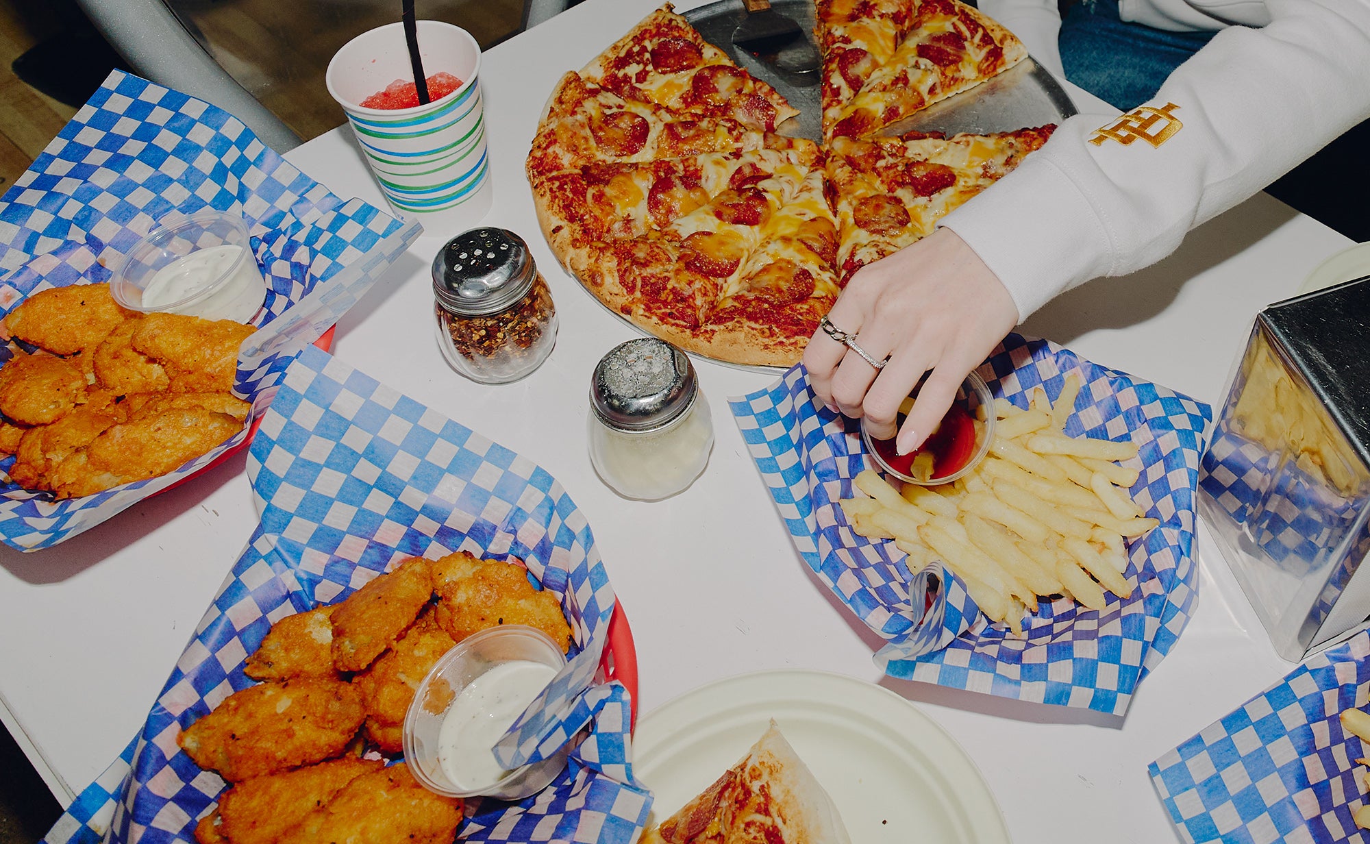 Table with pizza, chicken nuggets, fries, and drinks on checkered paper
